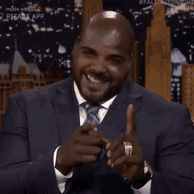 a man in a suit and tie is pointing at the camera while talking .