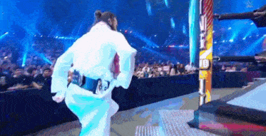 a man in a white robe is standing in a wrestling ring with a crowd watching .