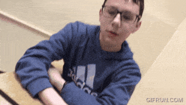 a boy wearing a blue adidas sweatshirt is sitting at a table