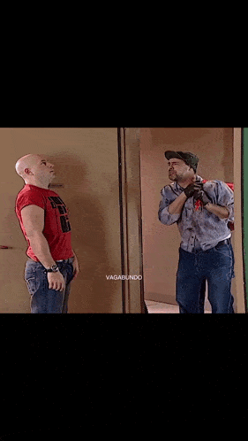 a bald man in a red shirt is standing next to a man in a hat .