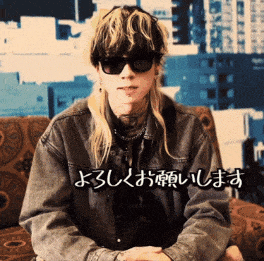 a man wearing sunglasses and a denim jacket is sitting on a couch in front of a wall with chinese writing on it