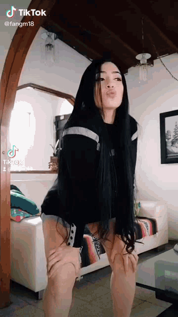 a woman with long black hair is standing in a living room with her hands on her knees