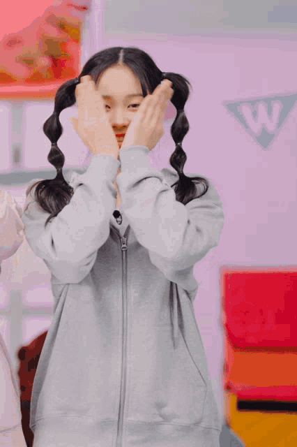 a girl with pigtails is wearing a gray hoodie with the letter w on it