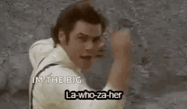 a man is standing in front of a wall with his fist in the air and says `` i 'm the big '' .