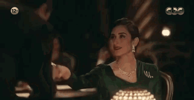 a woman in a green dress and necklace is sitting at a table in a restaurant .