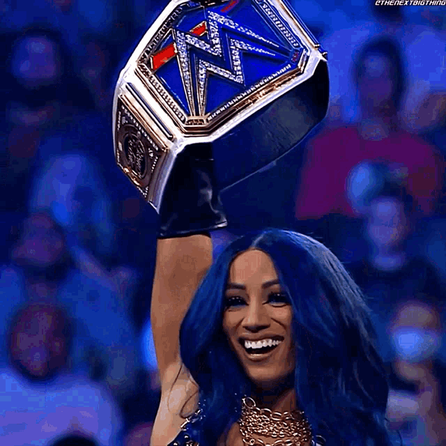 a woman with blue hair is holding a wrestling championship belt over her head