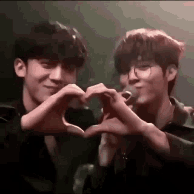 two boys are making a heart shape with their hands .