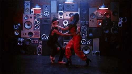 a man and woman dancing in front of a wall of speakers