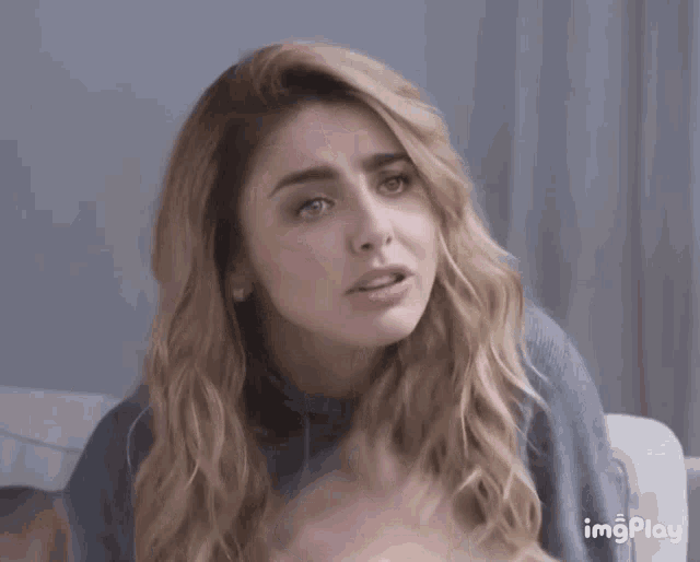 a woman with long blonde hair is sitting on a couch and looking at the camera with the words imgplay above her head