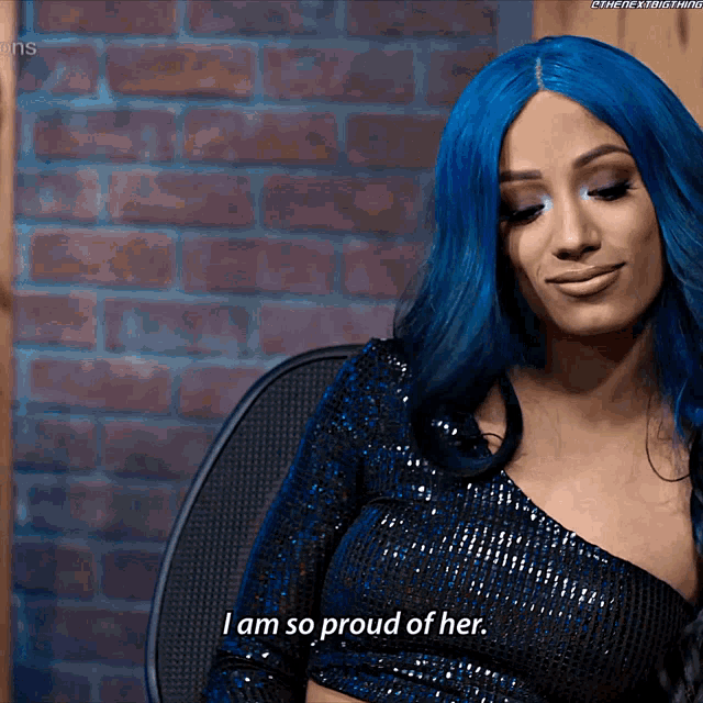 a woman with blue hair is sitting in a chair and says " i am so proud of her "