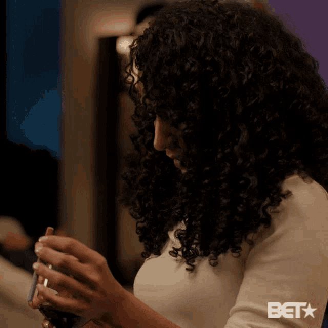 a woman with curly hair is looking at her phone with the bet logo in the corner