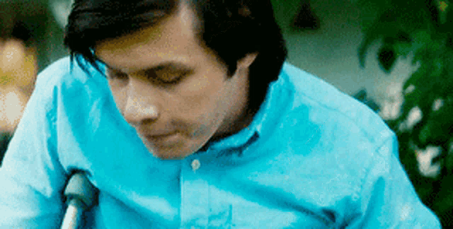 a man in a blue shirt is sitting in a wheelchair with crutches .