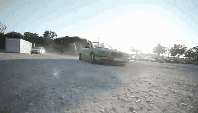 a green convertible car is driving down a dirt road