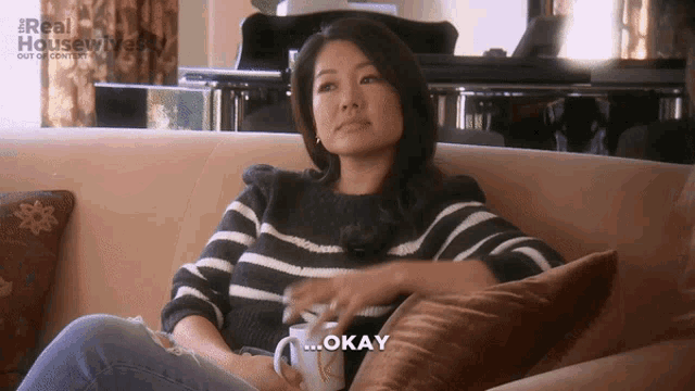 a woman is sitting on a couch with a cup of coffee and says okay