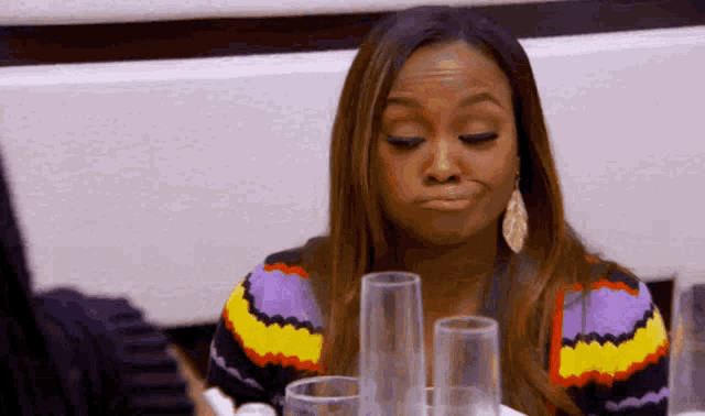 a woman in a colorful sweater is sitting at a table with glasses and making a funny face .
