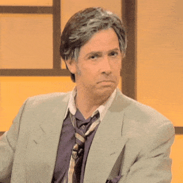 a man wearing a suit and tie is sitting in front of a yellow wall