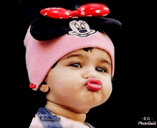 a baby wearing a pink minnie mouse hat blowing kisses