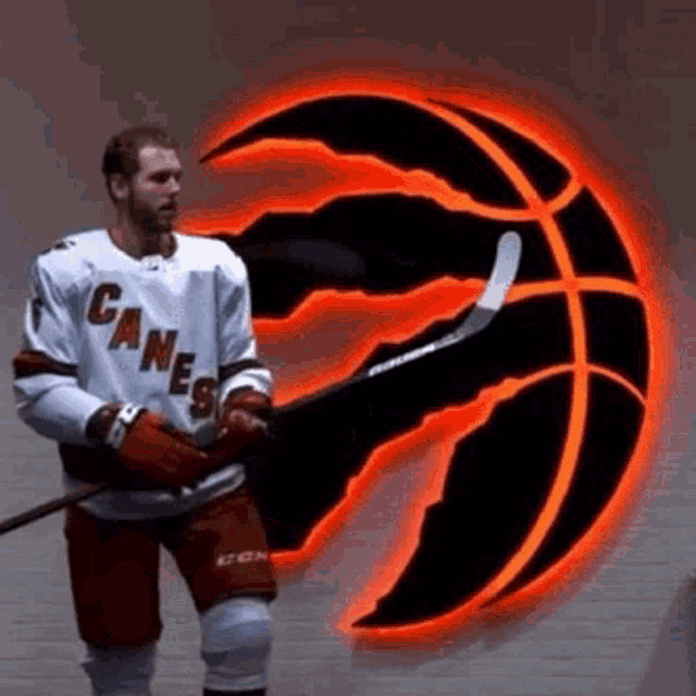 a man in a canes jersey is holding a hockey stick in front of a basketball