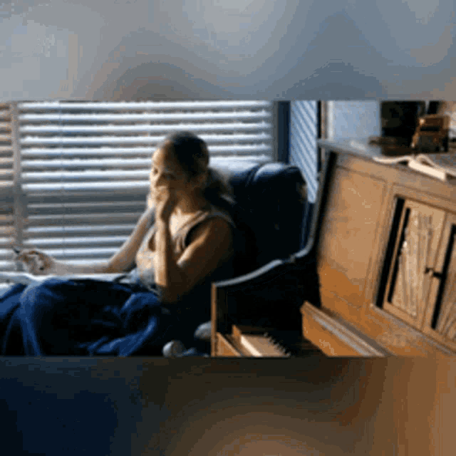 a woman is sitting in a chair in front of a window with blinds