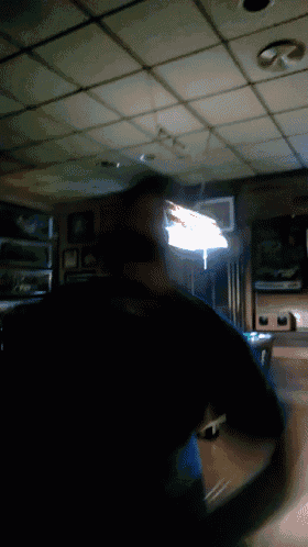 a man in a black shirt is standing in a dark room with a light on the ceiling