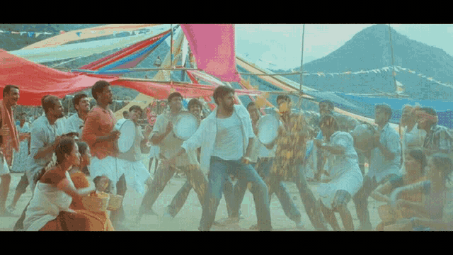 a group of people are dancing and holding drums in front of a mountain