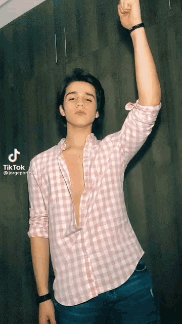 a young man wearing a pink plaid shirt has his fist in the air and a tiktok watermark