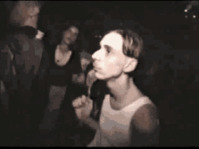 a man in a white tank top is dancing in a dark room with other people .