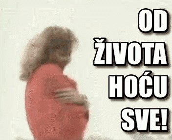 a woman in a red shirt is hugging herself in front of a white wall .