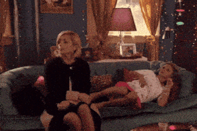 two women are sitting on a couch with a little girl laying on it