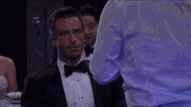 a man in a tuxedo and bow tie is standing next to another man .
