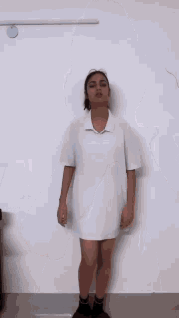 a woman wearing a white polo shirt dress is standing in front of a white wall .