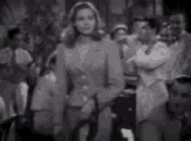 a black and white photo of a woman in a suit standing in front of a crowd .