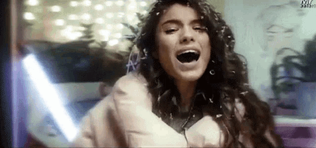 a woman with long hair is singing into a microphone while wearing headphones and a jacket .