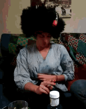 a woman wearing an afro wig is sitting on a couch taking a pill