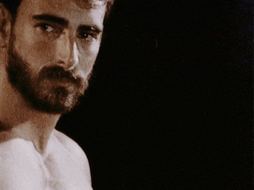 a man without a shirt has a beard and looks at the camera