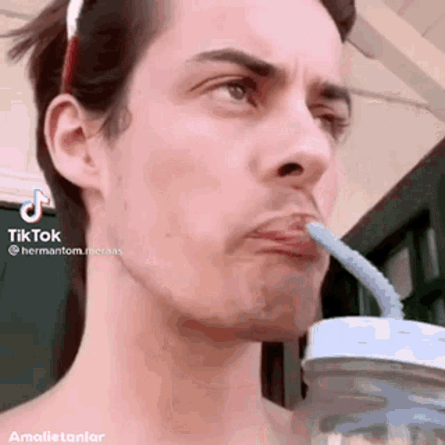 a shirtless man is drinking from a mason jar with a straw in his mouth .