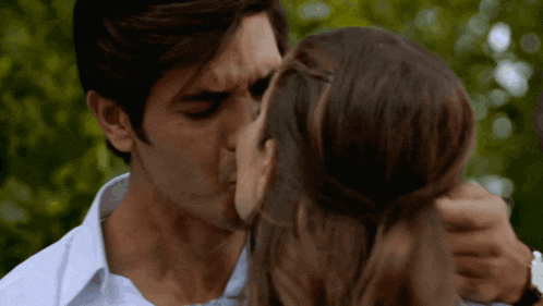a man kisses a woman on the cheek in front of a green background
