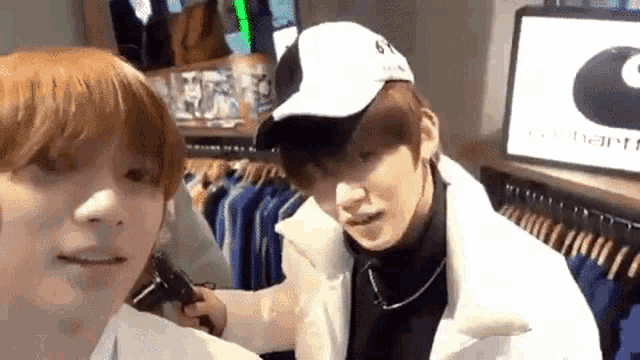 two men are standing next to each other in a clothing store . one of the men is wearing a baseball cap .