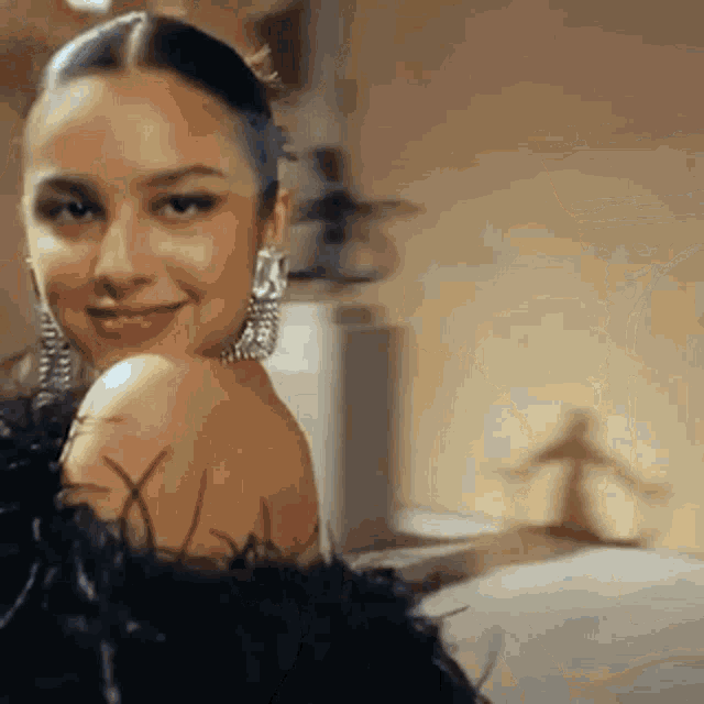 a woman in a black feathered dress is smiling and looking over her shoulder at the camera .