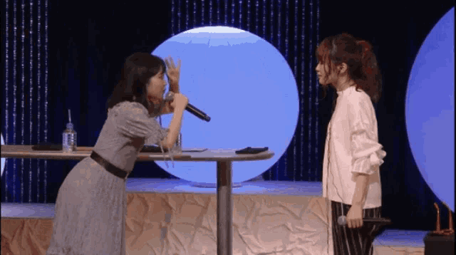 two women are standing next to each other on a stage with a microphone