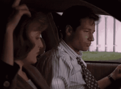 a man and a woman are sitting in a car . the man is wearing a tie and a striped shirt .