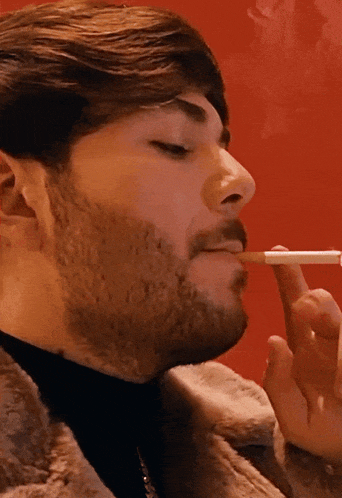 a man with a beard is smoking a cigarette against a red background
