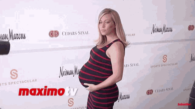 a pregnant woman is standing in front of a wall that has maximo tv written on it