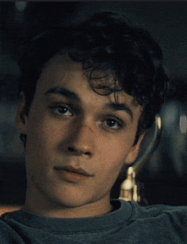 a young man with curly hair is wearing a grey sweatshirt