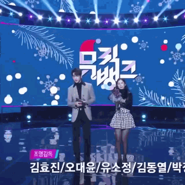 a man and a woman stand on a stage in front of a large screen with chinese characters