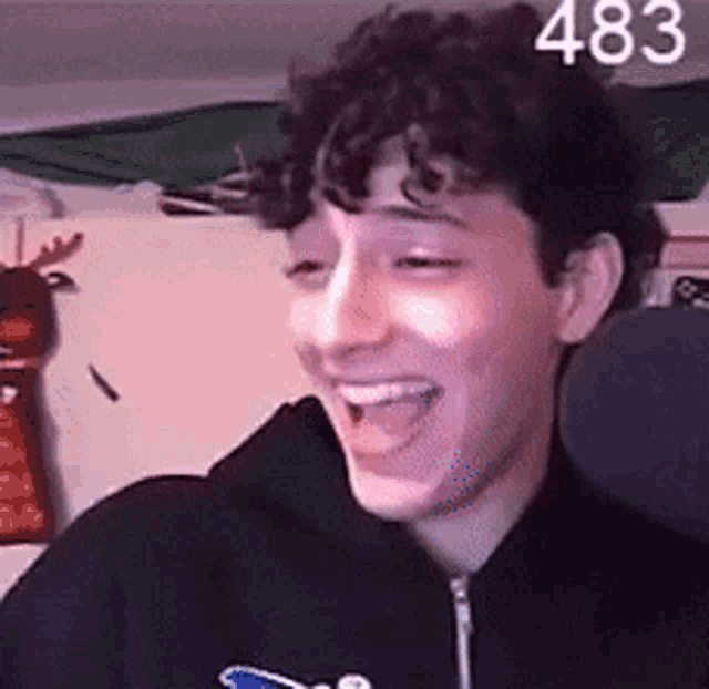 a young man with curly hair wearing a black hoodie is smiling .