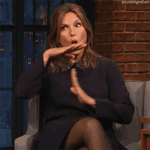 a woman in a black dress is sitting in a chair and making a funny face with her mouth open