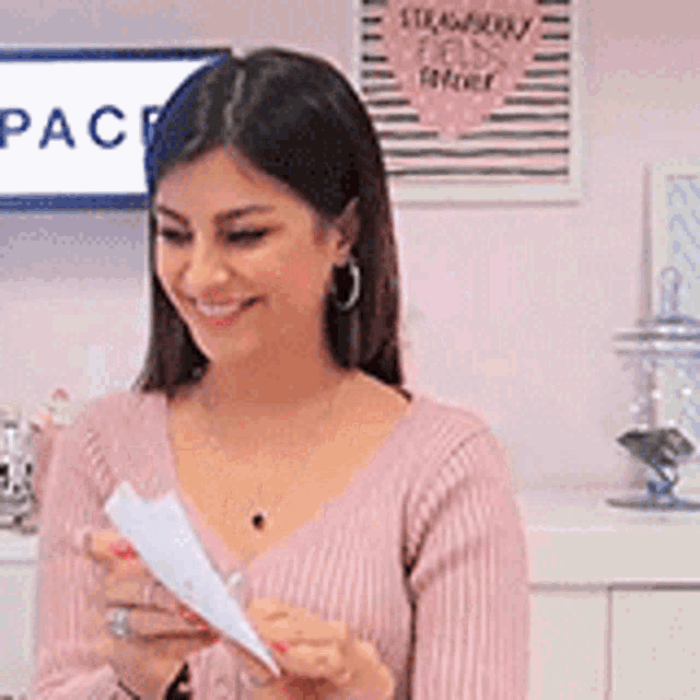 a woman in a pink sweater is holding a piece of paper in her hands .