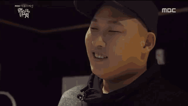 a man wearing a black hat and a gray sweater is talking to someone on a mbc tv show
