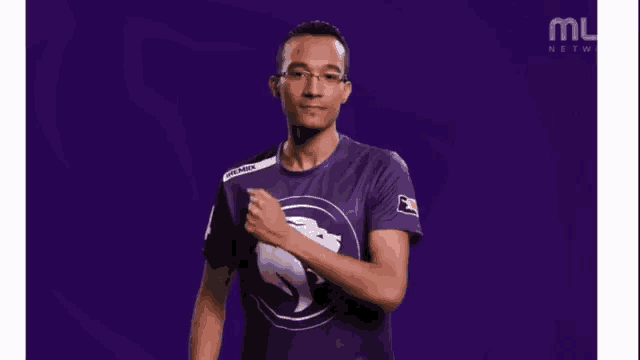 a man wearing a purple shirt with a white lion on it is pointing at his chest .
